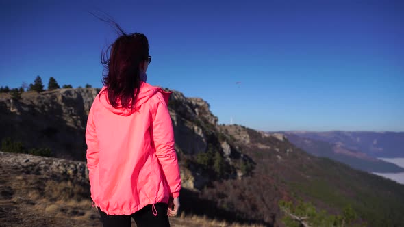 Young Redhead Woman Standing on a Rock High in the Mountains Above the Clouds and Enjoying the Warm