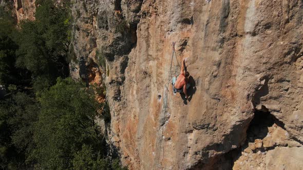 Aerial View From Drone of Strong Muscular Young Man Climbs on Big Rocky Wall By Challenging Rock