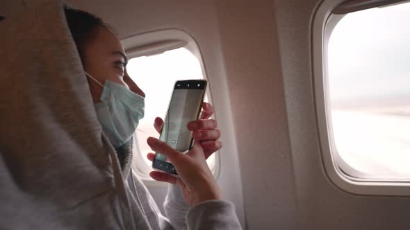 Happy Woman Tourist in Medical Face Mask Looking at Aircraft Window in Airplane Cabin