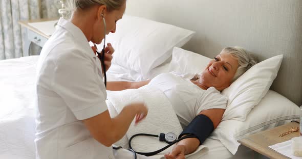 Female doctor checking the blood pressure of senior woman in the bedroom