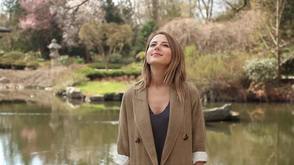 Young redhead woman stand near a lake in a garden