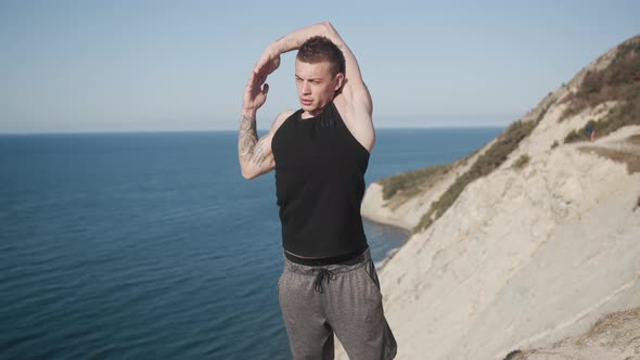 Tattooed Muscular Man Does Workout Outdoors at Sunny Day on Top of Mountain