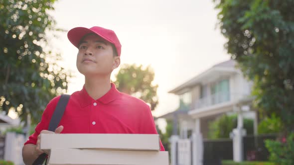 Asian postman in red color uniform handling bag of food, pizza walking and finding costumer house