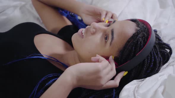 Close-up Face African American Girl with Dreadlocks Lying on White Bed and Listening To Music in