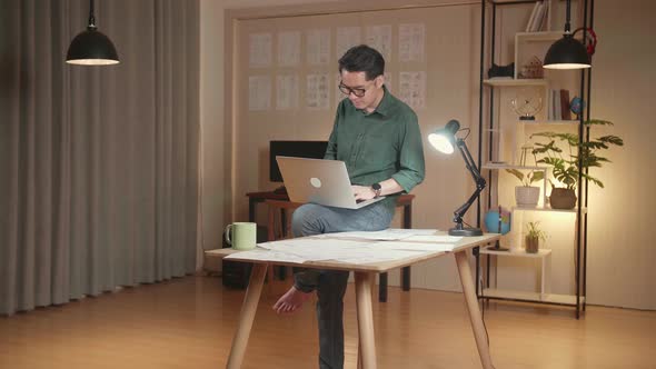 Creative Designer Sits On His Desk Holds Laptop On The Knees And Working On The Project