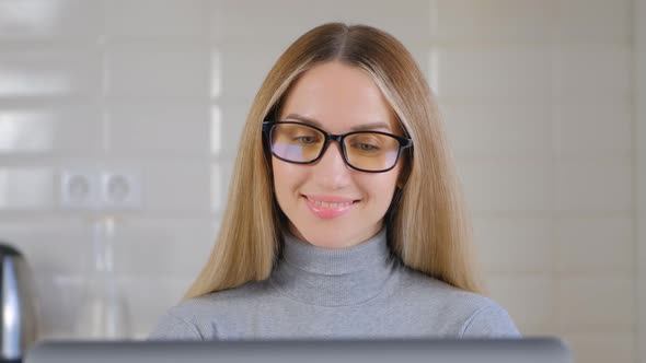 Portrait of cheerful blonde female typing text on notebook computer at home in 4k video