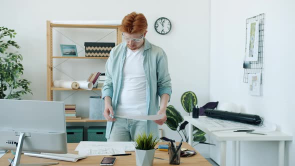 Slow Motion of Young Architect Looking at Blueprint Thinking Then Using Computer in Office