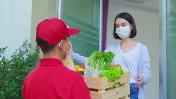 Asian deliver man wearing face mask in red uniform handling bag of food, groceries to woman customer