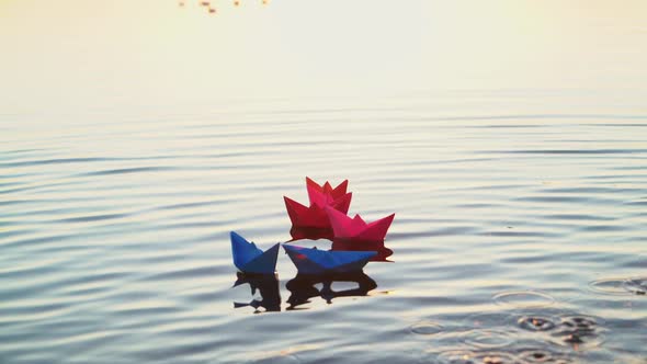 Toy paper boats on the surface water at sunset. Colored paper ships in the water