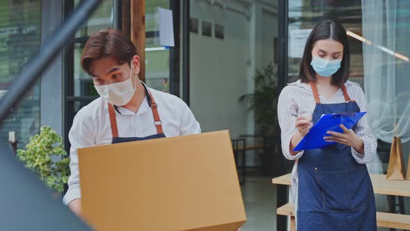 Asian waiter wear mask, loads parcels into car with waitress check on clipboard. Delivery Purchased.