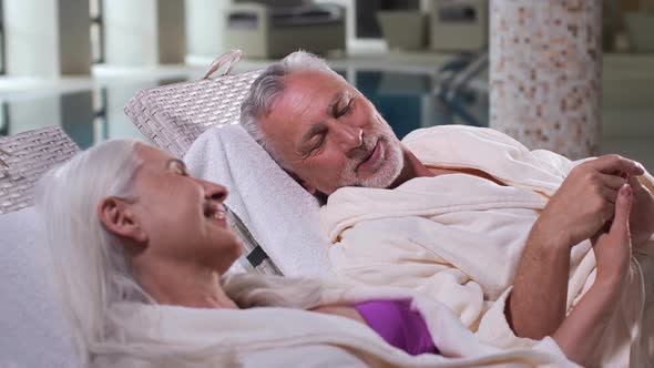 Elderly Couple Holding Hands Relaxing on Sunbeds