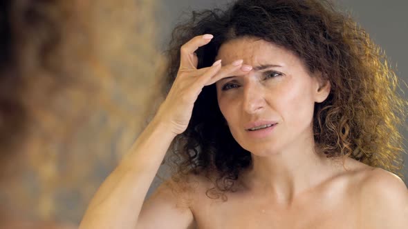 Middleaged Woman Regretfully Examines Her Wrinkles in the Mirror