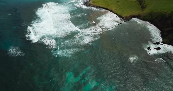 Drone shots of waves crashing on blue beach while panning up