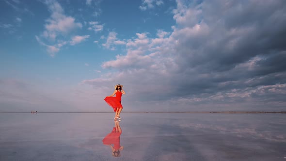 Woman Tourist in a Waving Dress Walks Along a Salt Lake in Which the Sky Is Reflected