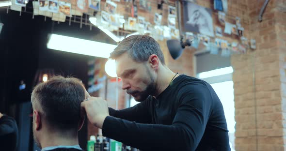 Professional Hairdresser Stylist Working with Scissors and a Comb Makes Haircut Client