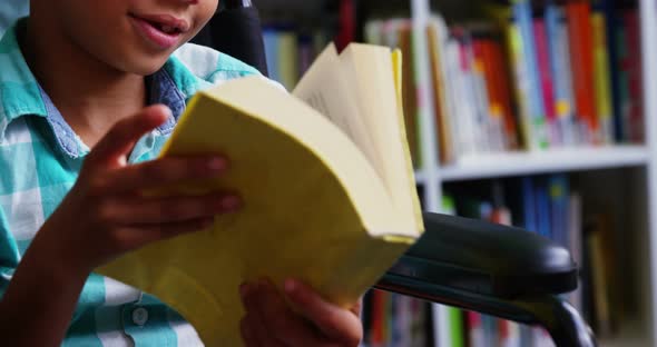 Disabled schoolboy reading book in library at school
