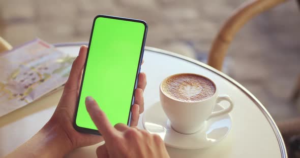 Crop View of Female Person Holding Mobilephone and Pressing on Greenscreen While Sitting at Table