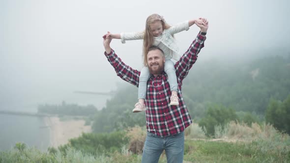 Happy Smiling Young Bearded Man Stretching Hands Holding Girl on Shoulders Talking Looking Away