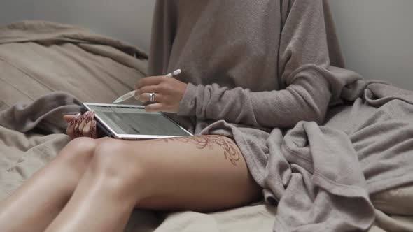 a Woman with a Henna Tattoo on Her Leg Scans Social Networks on a Tablet