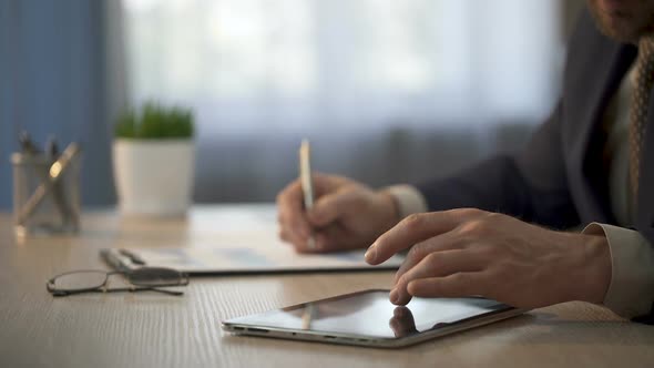 Company Worker Checking Information on Tablet to Mark Graphs, Statistical Report