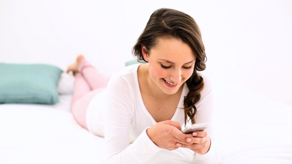 Smiling Woman Lying On Bed Texting On The Phone 2