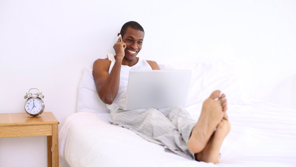Handsome Man Lying On Bed Phoning And Using Laptop