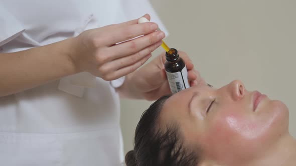 Applying Massage Oil on the Forehead of a Beautiful Brunette Woman in Spa Salon