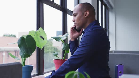 Mixed race businessman standing talking on smartphone looking out of window in office
