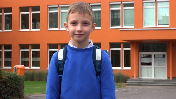 A Young Boy Smiles at the Camera - an Elementary School in the Background