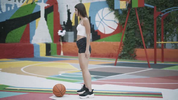 Wide Shot of Slim Young Woman Warming Up on Outdoor Basketball Court