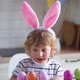 Cute two-year-old boy in bunny ears paint Easter eggs with multi-color paints sitting at the table - VideoHive Item for Sale