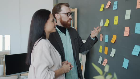 Business Team Girl and Guy Discussing Ideas Working with Sticky Notes on Office Wall