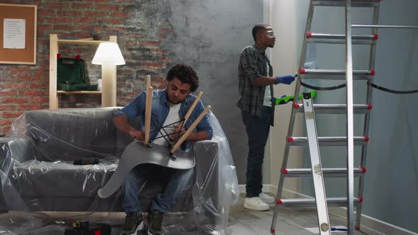 Black Man Paints Wall Guy Assembles Chair in Living Room