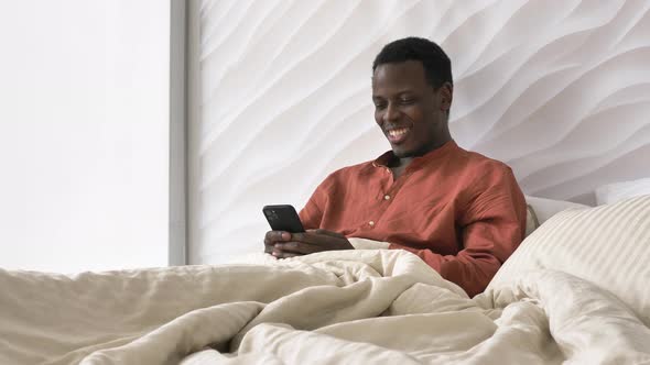 AfricanAmerican Man Laughs Reading Phone Message in Bed