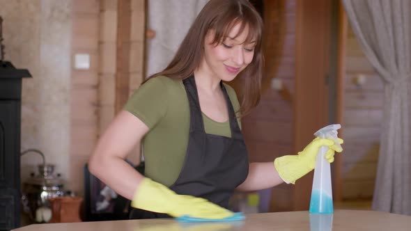 Handsome Woman Wipes Dust Off the Surface of Wooden Table with Microfiber Cloth