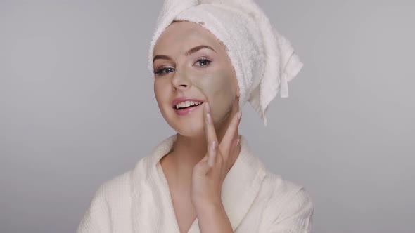 Girl in Bathrobe Applying Facial Clay Mask and Smoothes on Her Face