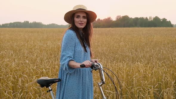 Portrait  girl in hat walking along rural road wheatfield on bike on summer day