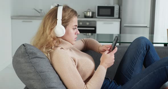 Relaxed Beautiful Young Woman Enjoying Music with Smartphone Enjoying Weekend While Lying on Sofa at