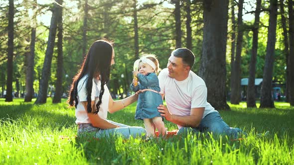 Pretty Toddler Girl with Parents Enjoy Summer on Green Grass in Sunny Park