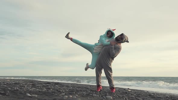 Man Is Lifting His Girlfriend, Both in Kigurumi and Standing on Beach Near Sea