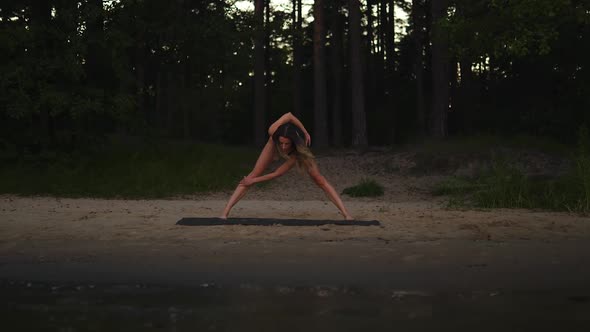 Evening Young Woman Practices Yoga on a Sandy Beach Using a Mat