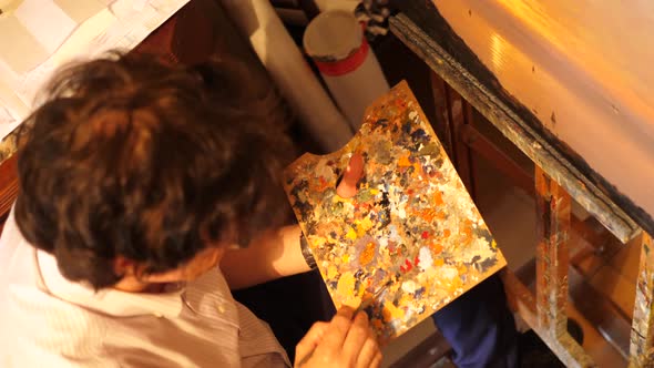 An artist paints an oil painting on canvas inside his art studio.