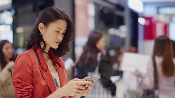 Asian woman hold out her smartphone and interacts with hand gestures on an unseen futuristic hologra