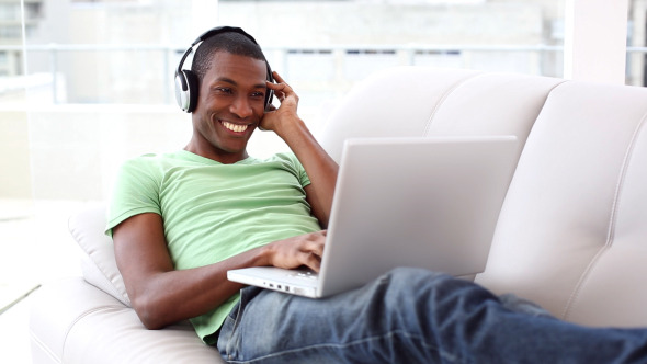 Smiling Man Lying On Couch Listening To Music