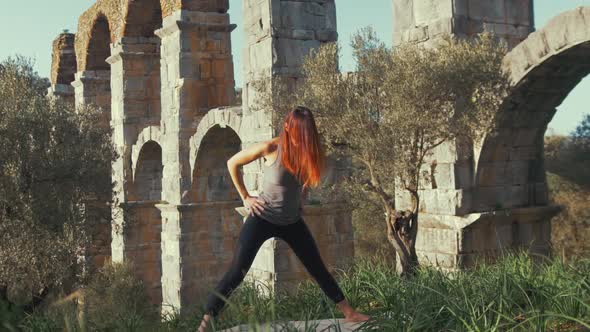 female athlete performing yoga routine stretching within wilderness at Ancient aqueduct