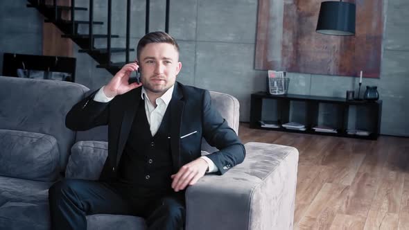 Handsome Man European Appearance in Classic Clothes in a White Shirt Sits in a Stylish Dark Office