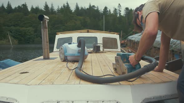 Carpenter sanding down roof planks of wooden liveaboard boat. MEDIUM WIDE SHOT