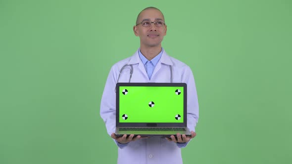 Happy Bald Multi Ethnic Man Doctor Thinking While Showing Laptop