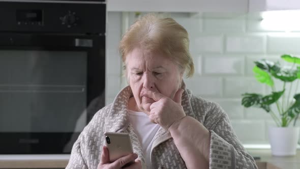 Sad Frustrated 70 Years Elderly Woman at Home Looking at Phone Seeing Bad News or Photos Feels