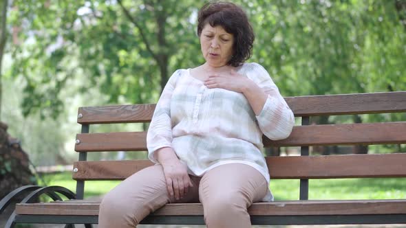 Stressed Senior Caucasian Woman Having Symptoms of Heart Attack in Sunny Summer Park. Portrait of
